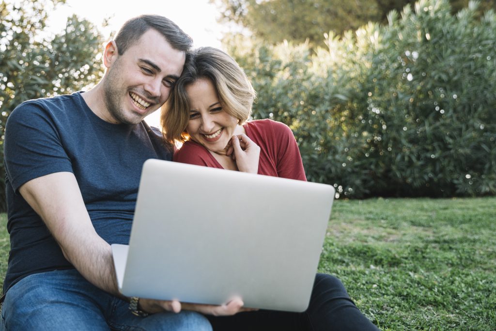 Casal feliz segurando um notebook, com um jardim ao fundo